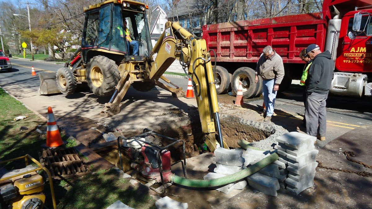 A repair crew with a backhoe excavating a street to reach the pipes below