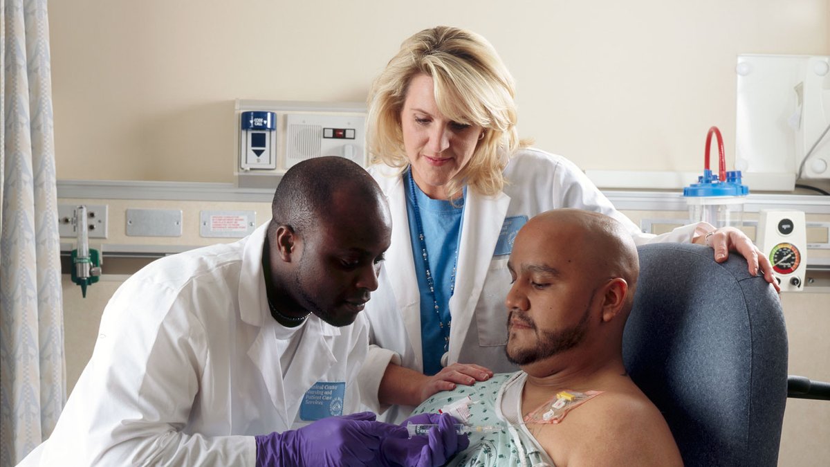 A patient receiving chemotherapy through a chest port while two clinicians attend