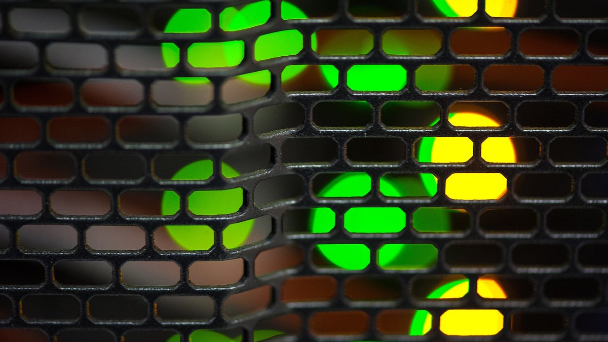 Server lights glowing green and amber behind a perforated panel in a data center