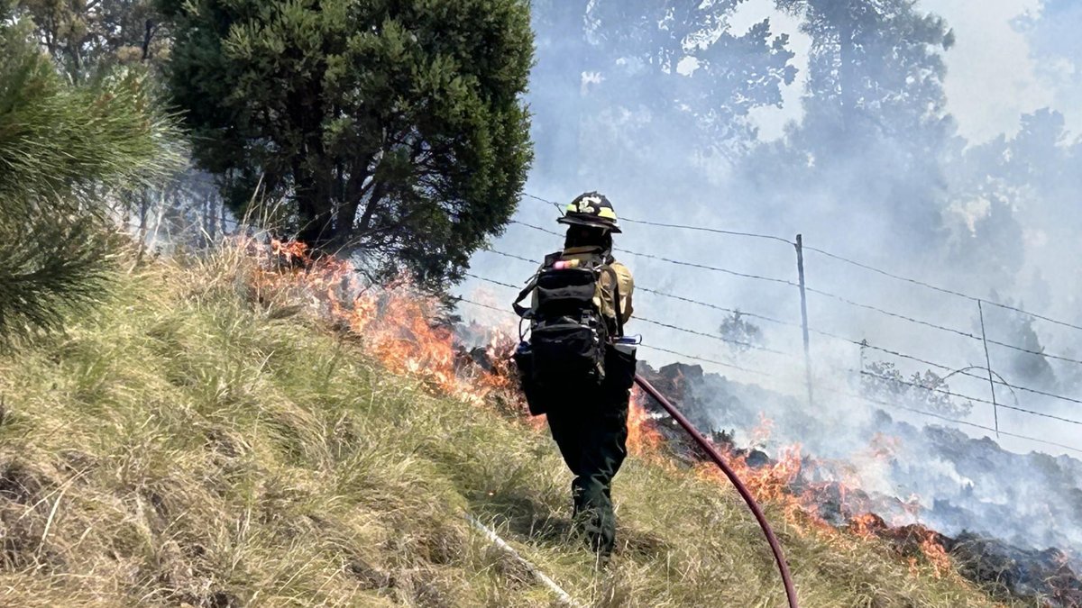 A firefighter working a hose line on a burning hillside near Ruidoso during the 2024 South Fork Fire