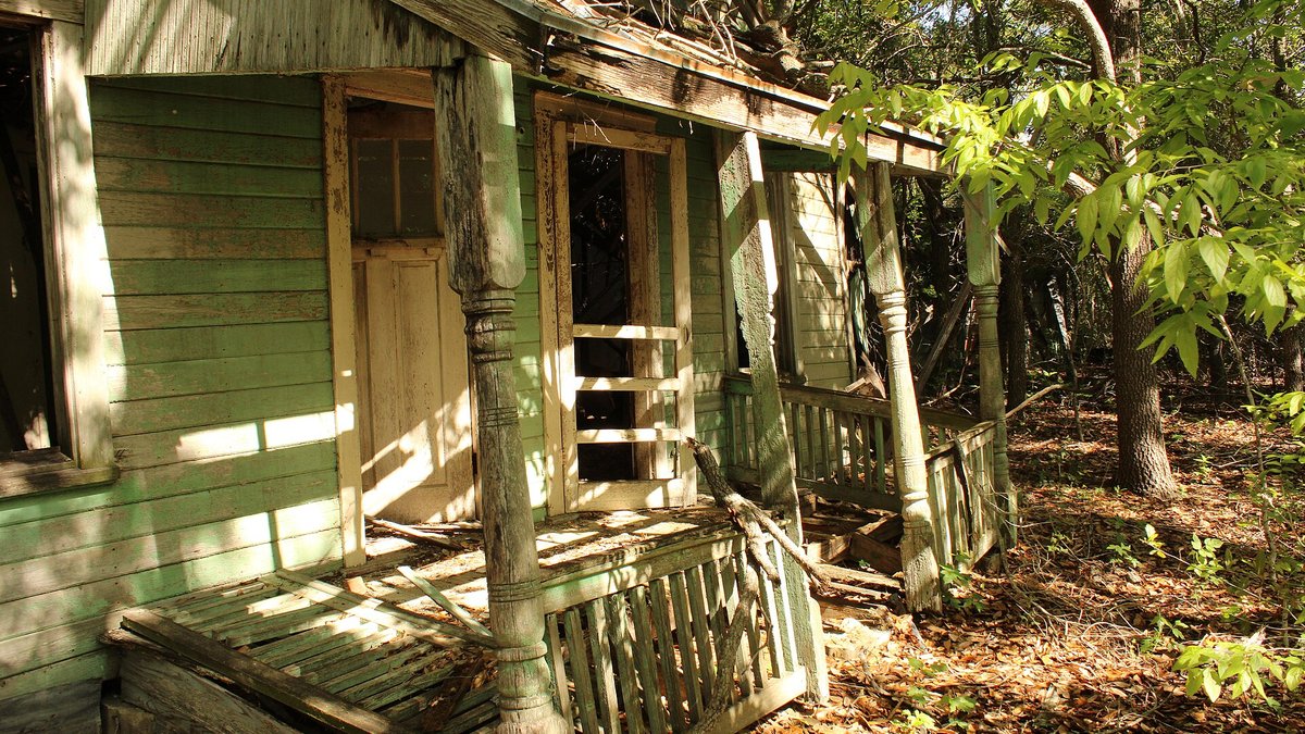 A vacant house with a collapsing porch, photographed in 2024